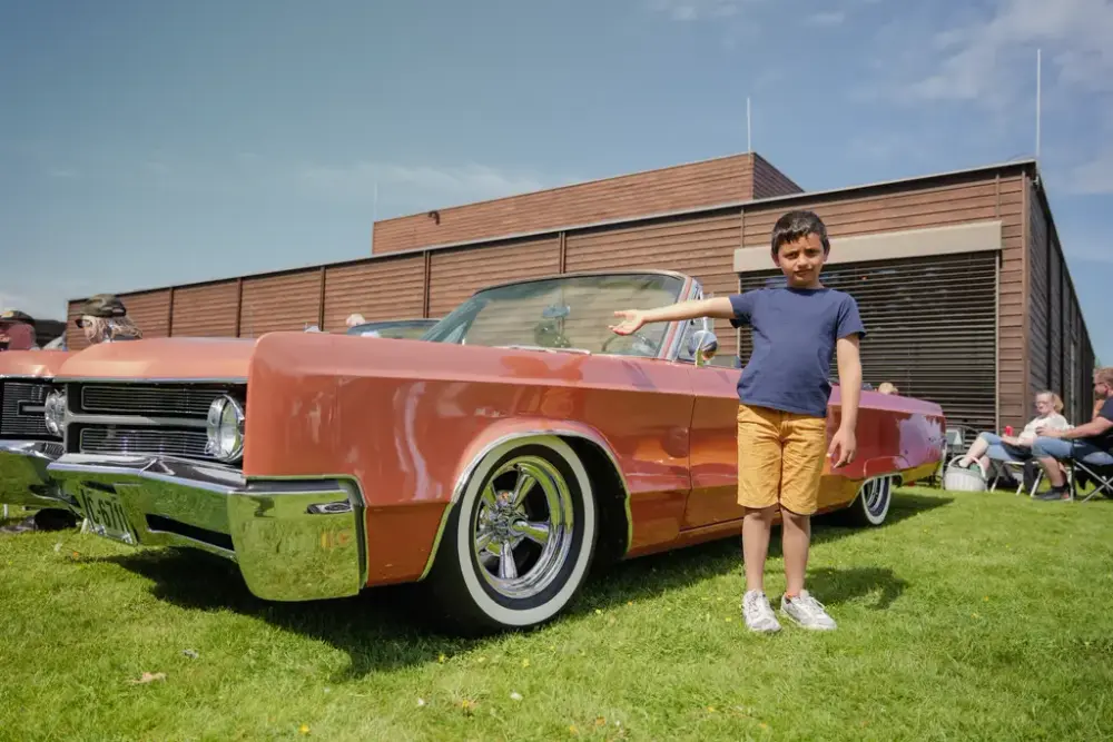 En gutt står og peker på en veteranbil.