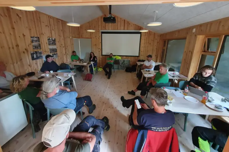 Flere personer sitter spredt i et møterom på hver sin stol