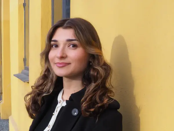 Portrett av en kvinne med mørkt hår foran en gul vegg.