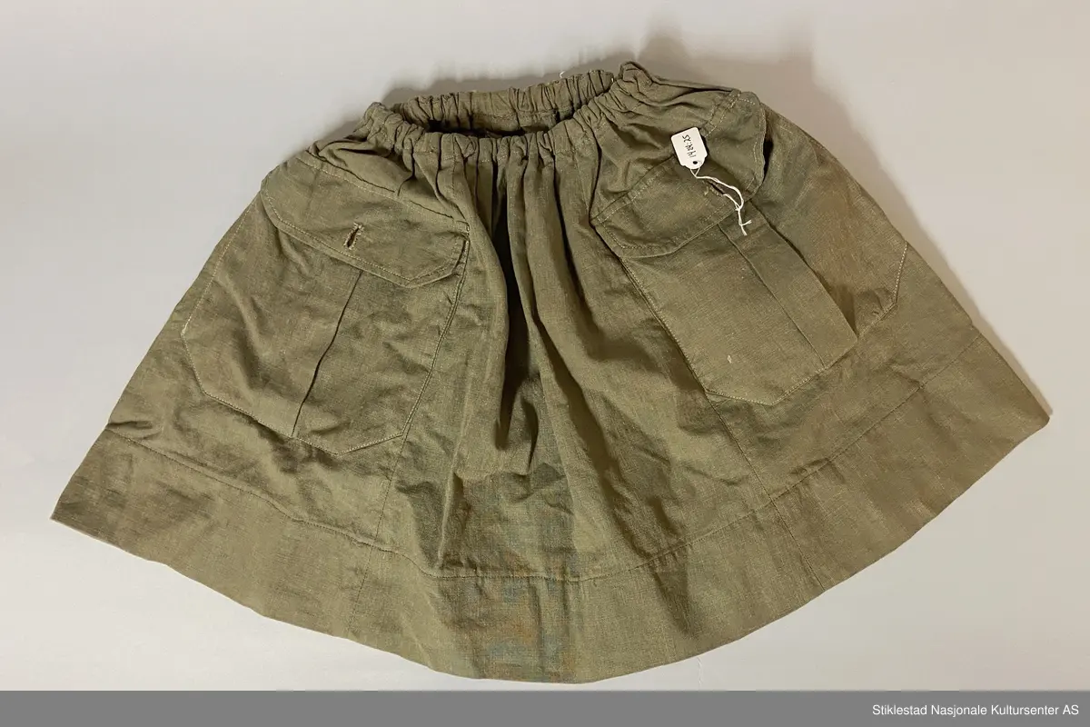 Speideruniform fra 1960-tallet. Dressen er i bomull og består av jakke, skjørt og lue (båtlue) i militærgrønn farge. Jakken har et påsydd stoffmerke på høyre arm: en blå trekant med trekløver og teksten KFUK - ("Kristelig Forening for Unge Kvinner"). På venstre skulderklaff er det festet et rødt bånd (dobbelt) med teksten «Verdal 1» (troppsgrad?). Rød snor i front for fløyte (denne mangler). Skjørtet er kort og "snurpet" sammen i midjen med strikk, to lommer foran. Merket K.K. på innsiden av ene lomme. Lue med påmontert merke i metall; trekløver i trekant. Innskripsjoner på innsiden av luen. Lue, militærgrønn, men annen grønn nyanse enn skjørt og jakke.