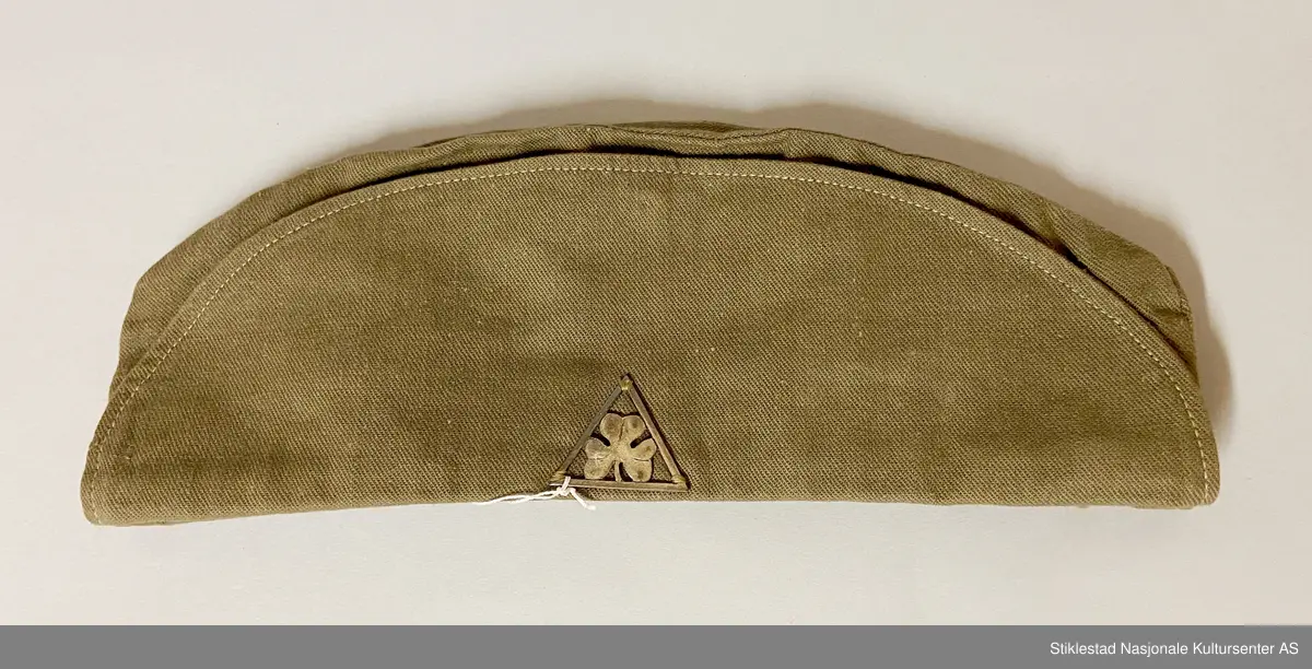 Speideruniform fra 1960-tallet. Dressen er i bomull og består av jakke, skjørt og lue (båtlue) i militærgrønn farge. Jakken har et påsydd stoffmerke på høyre arm: en blå trekant med trekløver og teksten KFUK - ("Kristelig Forening for Unge Kvinner"). På venstre skulderklaff er det festet et rødt bånd (dobbelt) med teksten «Verdal 1» (troppsgrad?). Rød snor i front for fløyte (denne mangler). Skjørtet er kort og "snurpet" sammen i midjen med strikk, to lommer foran. Merket K.K. på innsiden av ene lomme. Lue med påmontert merke i metall; trekløver i trekant. Innskripsjoner på innsiden av luen. Lue, militærgrønn, men annen grønn nyanse enn skjørt og jakke.