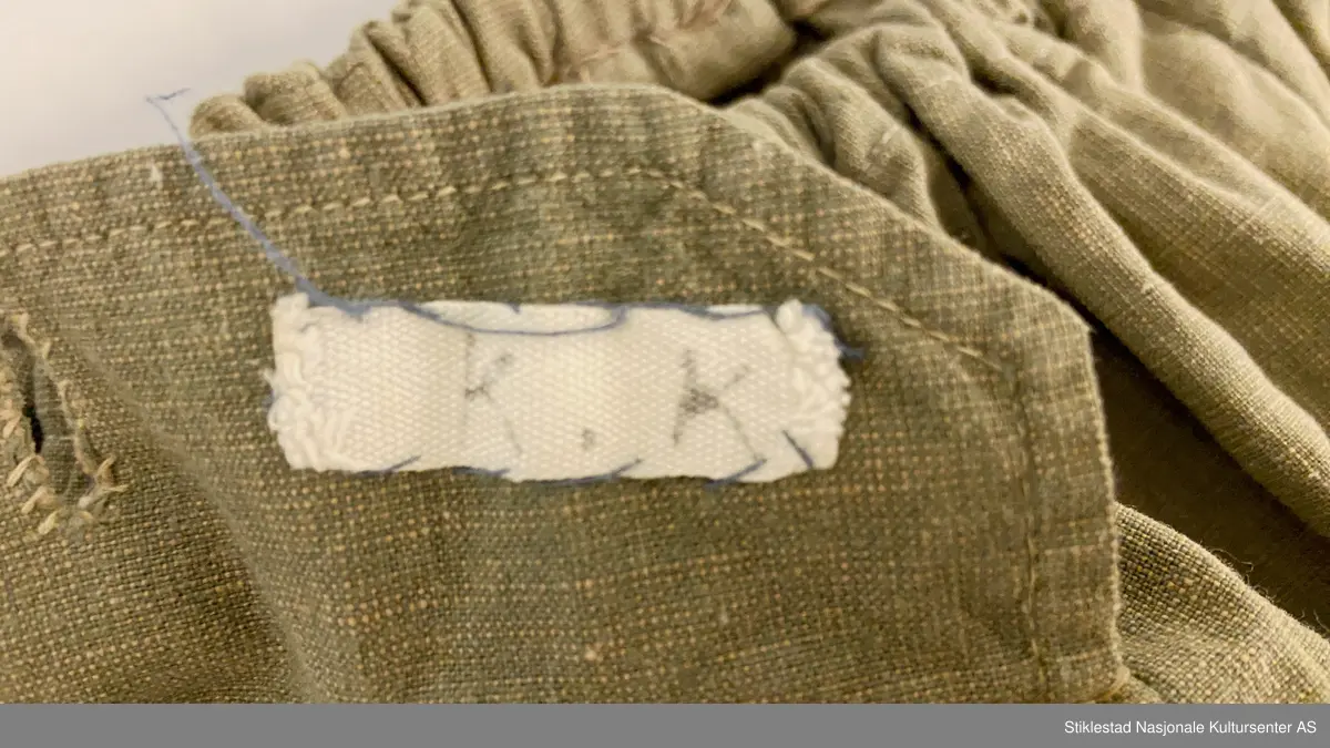 Speideruniform fra 1960-tallet. Dressen er i bomull og består av jakke, skjørt og lue (båtlue) i militærgrønn farge. Jakken har et påsydd stoffmerke på høyre arm: en blå trekant med trekløver og teksten KFUK - ("Kristelig Forening for Unge Kvinner"). På venstre skulderklaff er det festet et rødt bånd (dobbelt) med teksten «Verdal 1» (troppsgrad?). Rød snor i front for fløyte (denne mangler). Skjørtet er kort og "snurpet" sammen i midjen med strikk, to lommer foran. Merket K.K. på innsiden av ene lomme. Lue med påmontert merke i metall; trekløver i trekant. Innskripsjoner på innsiden av luen. Lue, militærgrønn, men annen grønn nyanse enn skjørt og jakke.