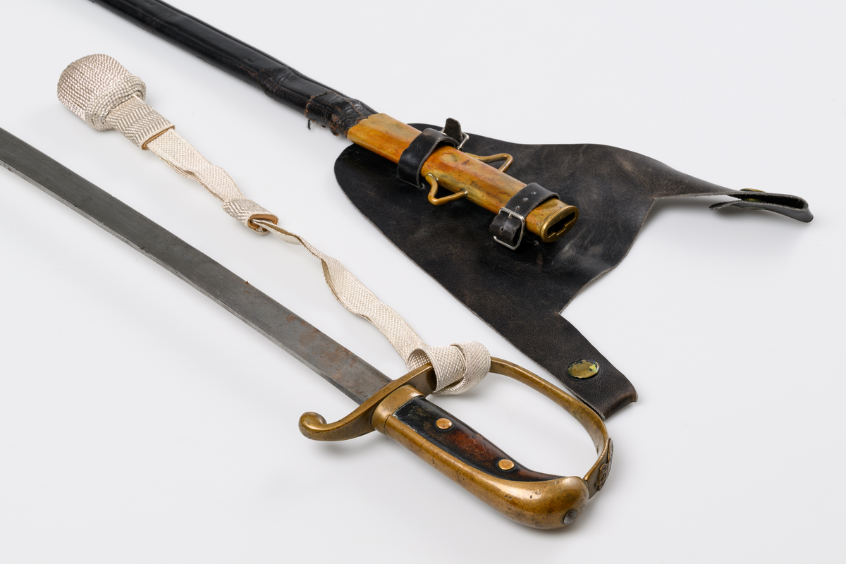 Polissabel m/26 med bäranordning. Handbygel och parérstång i förgylld mässing. Polisemblem på handbygeln. Kavel i läder. Handbygeln har en s.k. portepé i silverdrageri. Klinga i stål. Sabelbalja av läder, munbleck och beslag med släpsko i förgylld mässing.