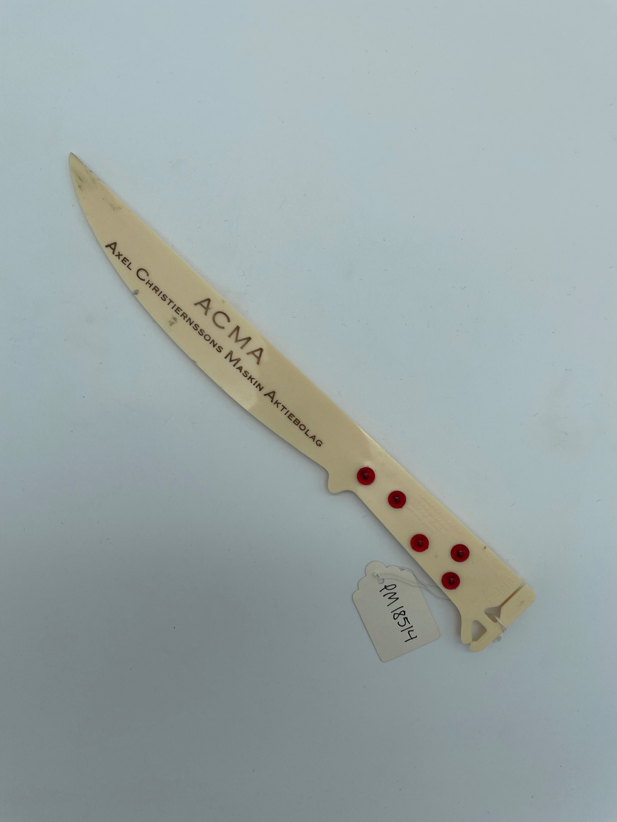 Brevkniv i plast med text i guld: "ACMA Axel Christiernssons Maskin Aktiebolag".

Brevkniven kan också användas som brevvåg. Det finns ett jack i ena änden där man kan klämma fast ett brev (text: Insert letter) och 5 stycken röda knappar som går att snurra på. Knapparna har olika viktangivelser (5g, 10g, 20g, 40g och 50g) för att mäta brevets tyngd. Man klämmer fast brevet och håller med tum och långfinger om en knapp för att hitta jämnvikt. Se bild två.

Brevkniven fungerar även som linjal. Längs brevknivens ena långsida finns en måttstock med mm-skala (0-18 cm).