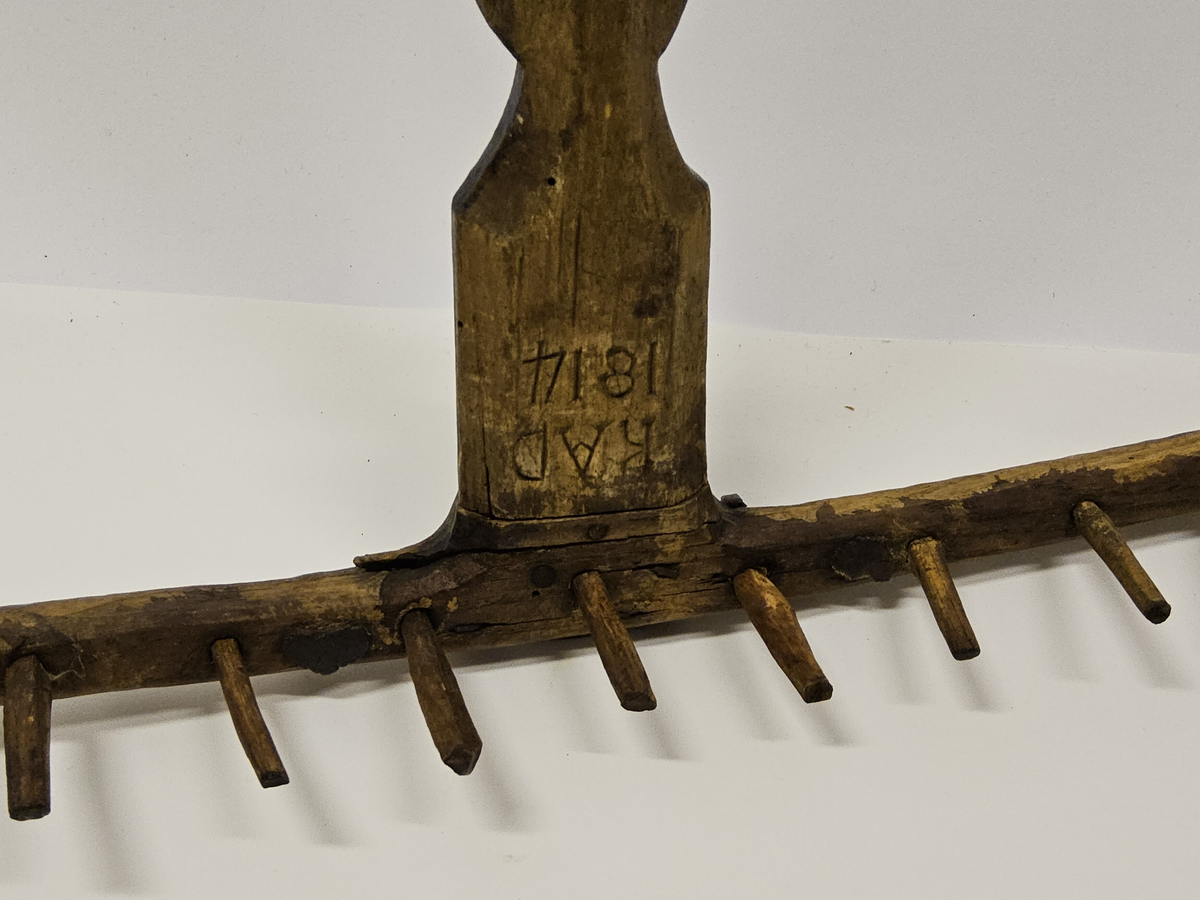 Räfsa med helt skaft. Rika sniderier, bl.a. rosett i karvsnitt samt stiliserade bladornament. På undersidan järnvägslatpp "Skultorp". Inköpt på auktion.