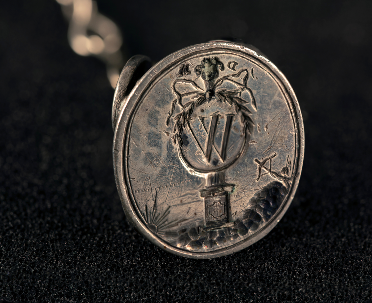 Lommeur med kjede av fire lenker og fem kjeder med anheng. Kjede med signet W, en oval medaljong med to kryssede fakler (WFA), en tannpirker formet som nøkkel, en mynt (F III 1666), firkantet uropptrekker. Stempel: se foto.