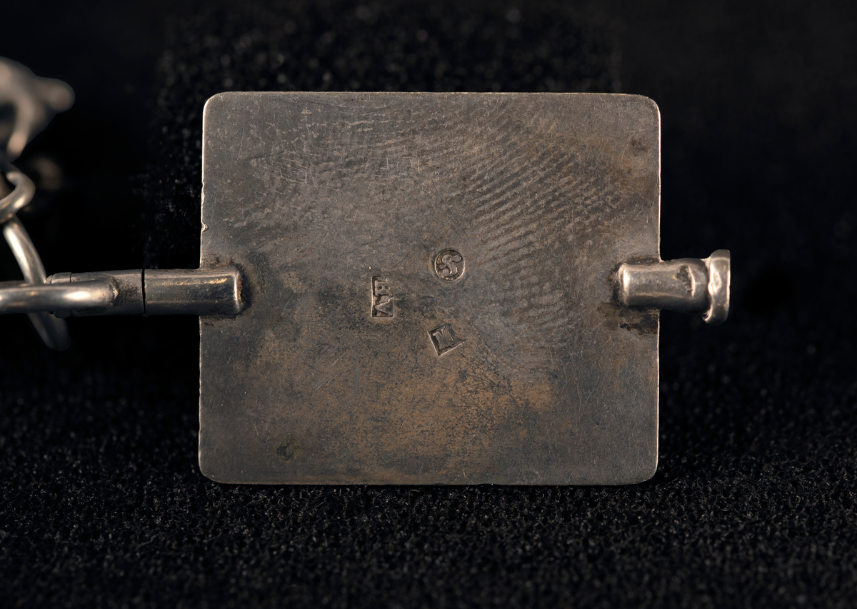 Lommeur med kjede av fire lenker og fem kjeder med anheng. Kjede med signet W, en oval medaljong med to kryssede fakler (WFA), en tannpirker formet som nøkkel, en mynt (F III 1666), firkantet uropptrekker. Stempel: se foto.