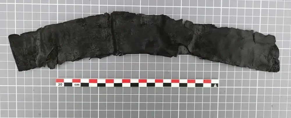 Buet lærfragment fra en middelaldersk sverdslire, mørkt og delvis slitt, med synlig søm og spor etter bruk.