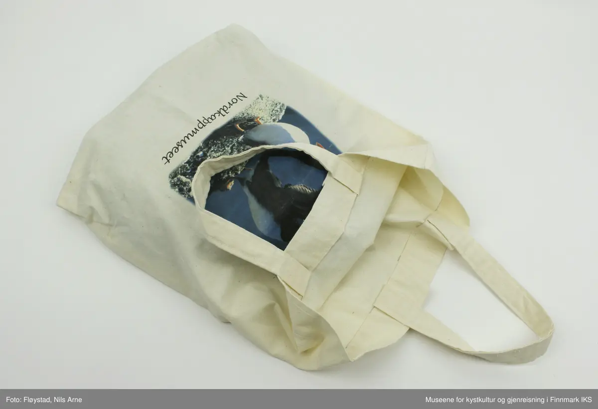 En hvit souvenirveske dekorert med tekstiltrykk. Vesken er laget av bomull og sydd med maskinsøm. 

Tesktiltrykket er et fargebilde av to lundefugler på et berg, den ene fuglen flakser med vingene mens den andre har vingene hvilende inntil kroppen. Under bildet er "Nordkappmuseet" trykt i sort skrift.