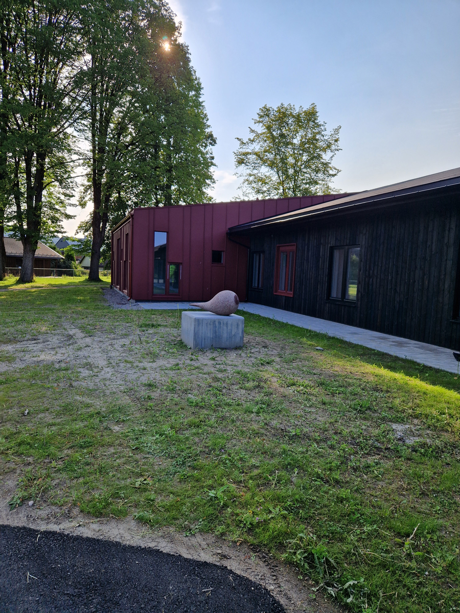 Skulptur utført i rød granitt. 140 cm lang med en tykk, rund del på ca 80 cm diameter og med en tynnere «hale». Et parti i den runde delen er polert slik at rødfargen er fremtredende.  