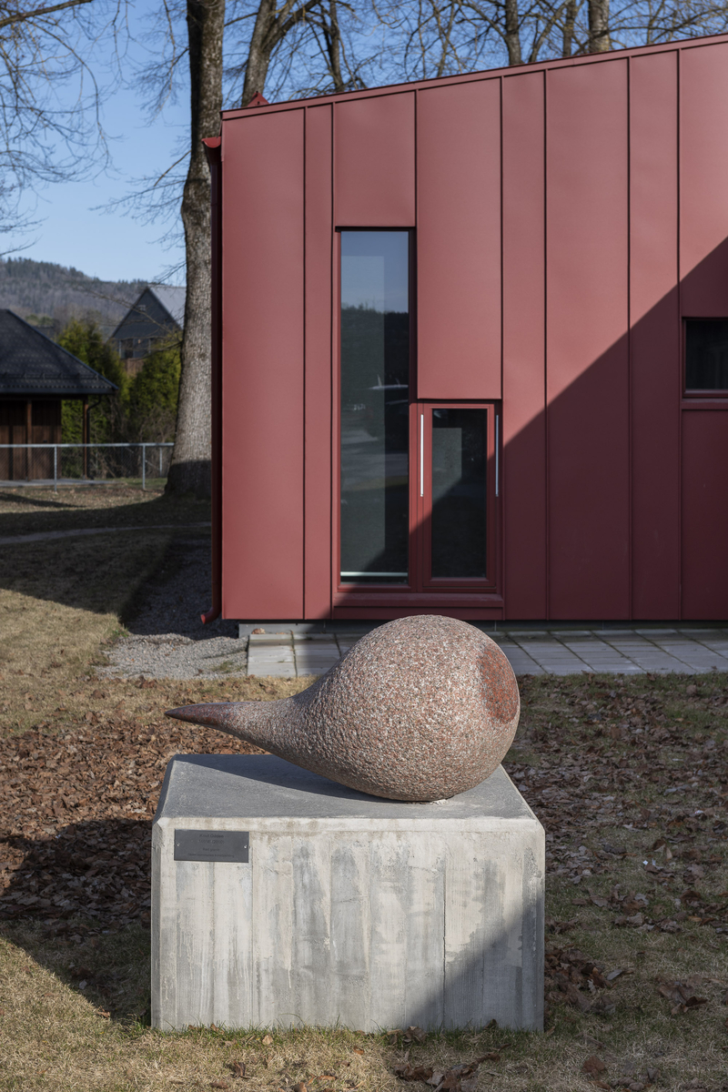 Skulptur utført i rød granitt. 140 cm lang med en tykk, rund del på ca 80 cm diameter og med en tynnere «hale». Et parti i den runde delen er polert slik at rødfargen er fremtredende.  