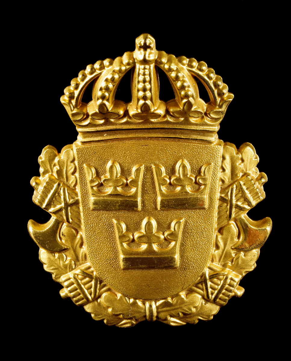 Mössplåt för polis. Sköld med lilla riksvapnet (tre kronor) med två bakomliggande fasces och ekkrans, krönt med kunglig krona. På frånsidan en fästskruv för montering.