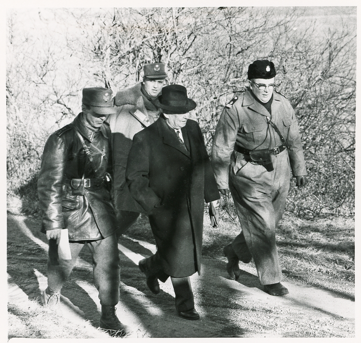 Några herrar vandrar längs en grusväg. I mitten landshövding Thorwald Bergquist och t.h. kommissarie Sture Sandell. De övriga okända.
Spaning efter "Jack" någonstans i Kronobergs län, 1959. Reportagebild.