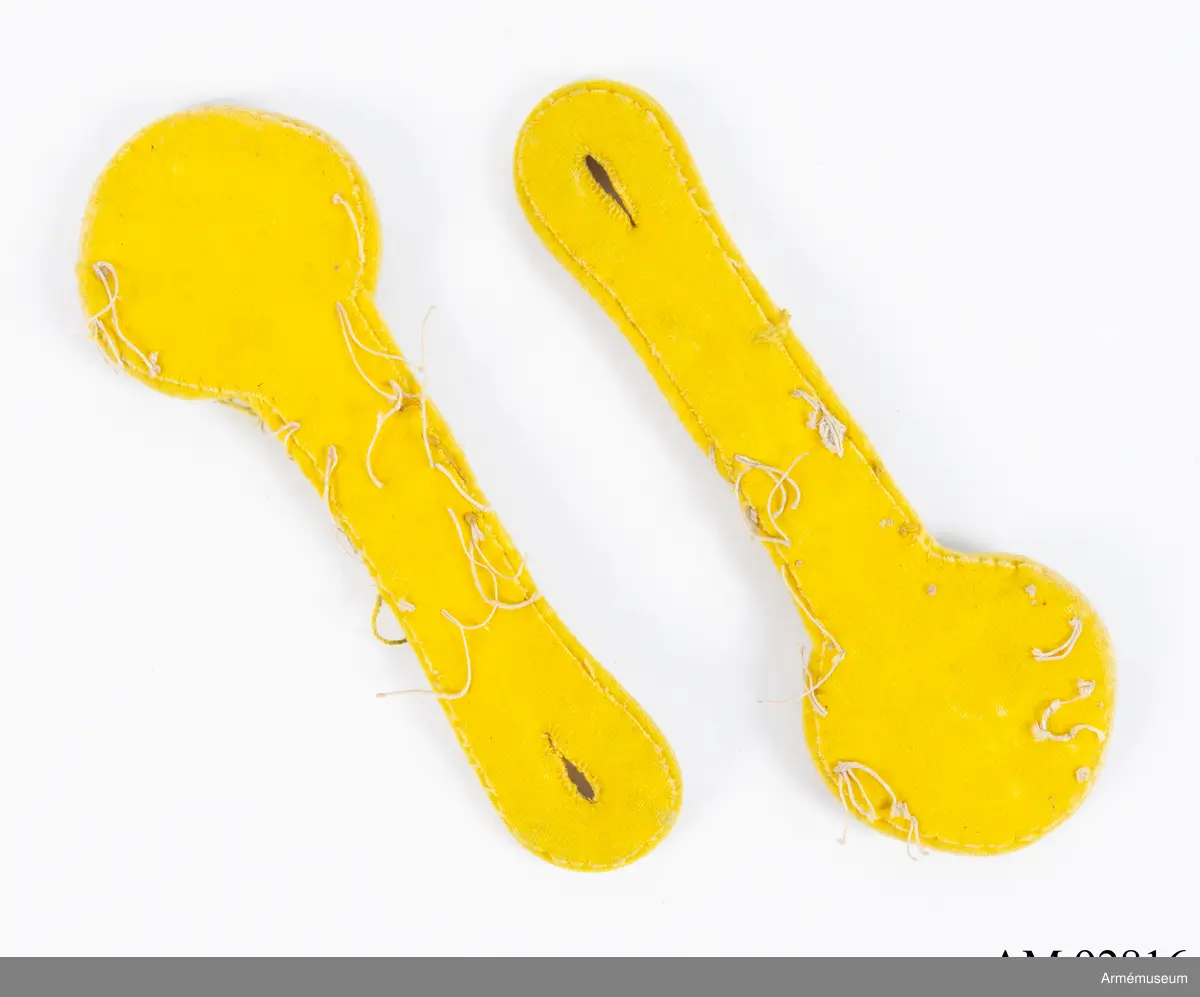 Ett par axeltränsar i silver på gul botten med guldfärgade metalldekorationer.

Axeltränsarna är gjorda av dubbelt silverfärgat beläggningssnöre av metalltråd i en platt flätad form med tre dubbla knutor och en stjälk vars ögla bildar ett knapphål. Ovanpå den flätade formen är fastsytt två femuddiga stjärnor samt en 1:a i mässing.
Allt samman är sedan fastsytt på en botten av gult kläde i vars kanter syns rester av oblekt lingarn som visar att tränsarna sprättats loss från axlarna på en uniform.