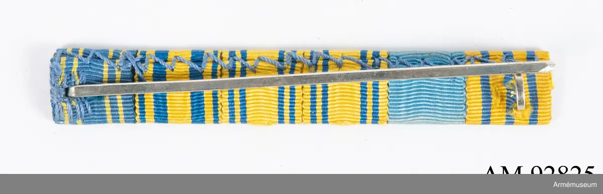 Släpspänne med ordensband från diverse svenska ordnar.

Spännet består av ett långsmalt metallbakstycke med band från 6 olika svenska ordnar eller minnestecken monterade på framsidan. På baksidan en nål för fastsättning.
