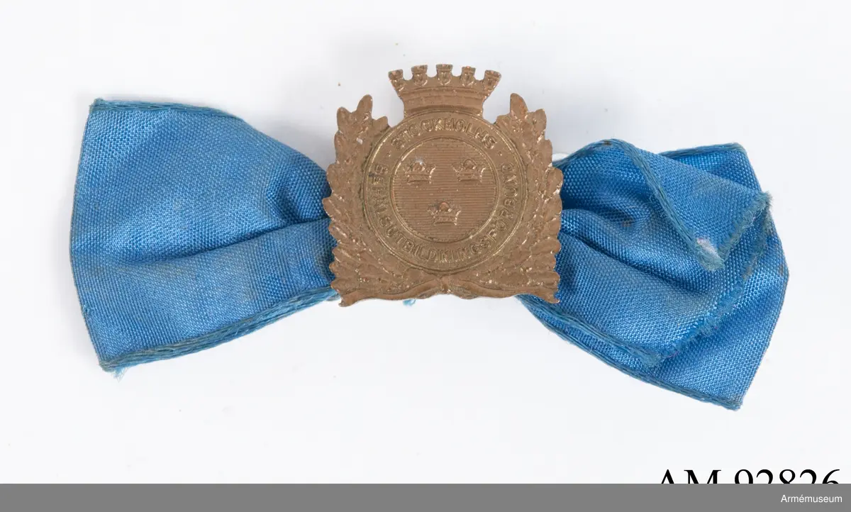 Blå rosett med bronsmedalj för Stockholms befälsutbildningsförbund.

Medaljen är tillverkad i brons. Framsidan har en rundel med tre kronor på räfflad botten inom ett cirkelrunt band med texten "Stockholms befälsutbildningsförbund", omgivet av ekkvistar och en krona. Märket har en nål på baksidan som i sin tur är fäst i en blå sidenrosett med en säkerhetsnål på baksidan.