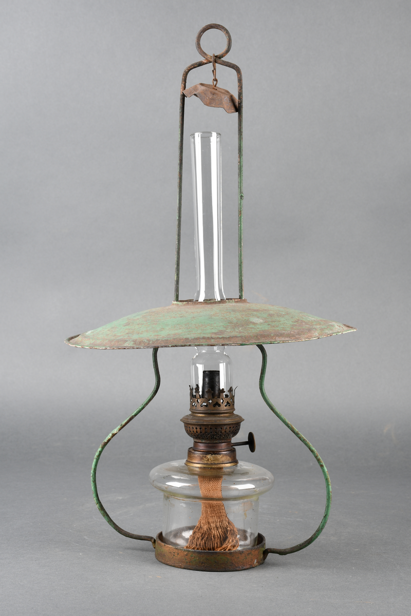 Oljelampe bestående av stativ av metall, skjerm av blikk malt grønn på oversiden og hvit på undersiden, parafinbrenner av glass, metall og veke av vevet tekstil, samt et lampeglass.