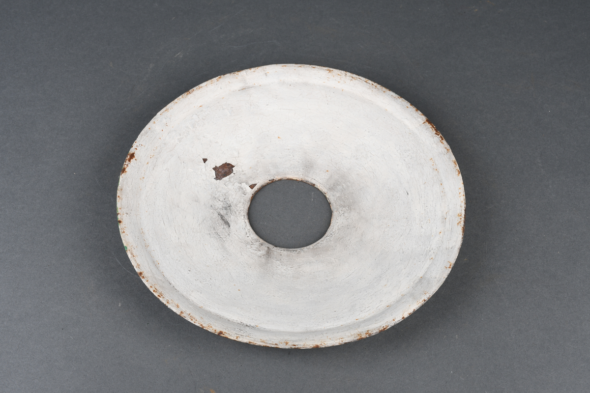 Oljelampe bestående av stativ av metall, skjerm av blikk malt grønn på oversiden og hvit på undersiden, parafinbrenner av glass, metall og veke av vevet tekstil, samt et lampeglass.