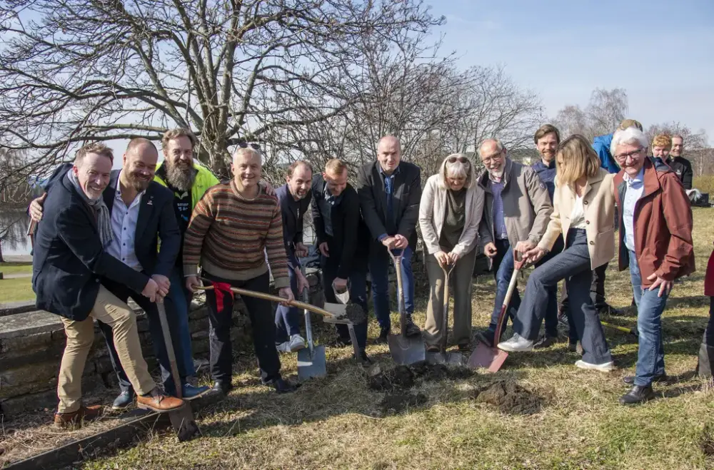 En stor gruppe mennesker, står med spader ned i jorden og smiler