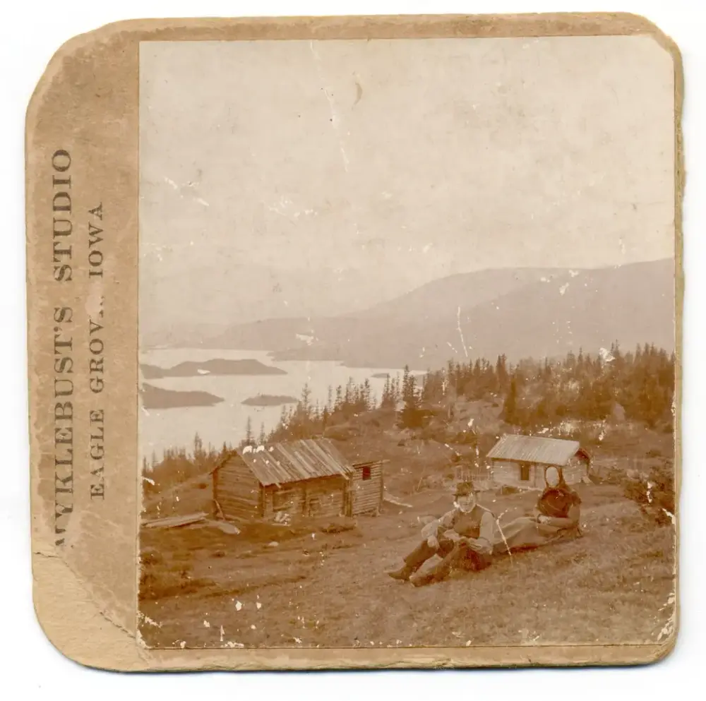 Husmannsplass med gamle hus, og eit sittande par i kulturlandskapet