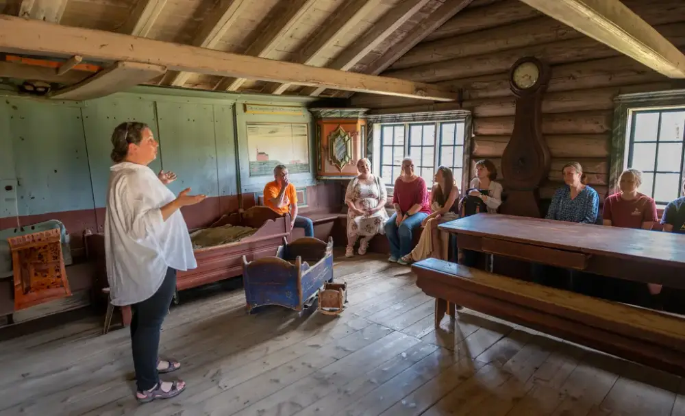 Omvisning i historisk stue med guide og besøkende sittende langs veggene.