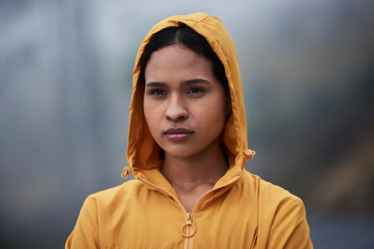 En ung kvinne med gul regnjakke og hette trukket over hodet