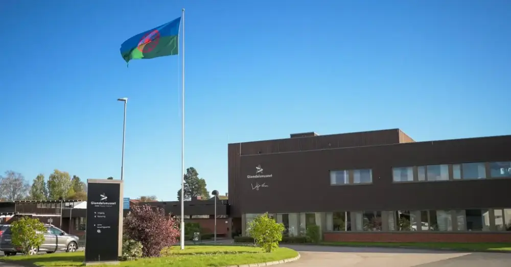 Museumsbygning utendørs med flaggstang og inngangsparti.