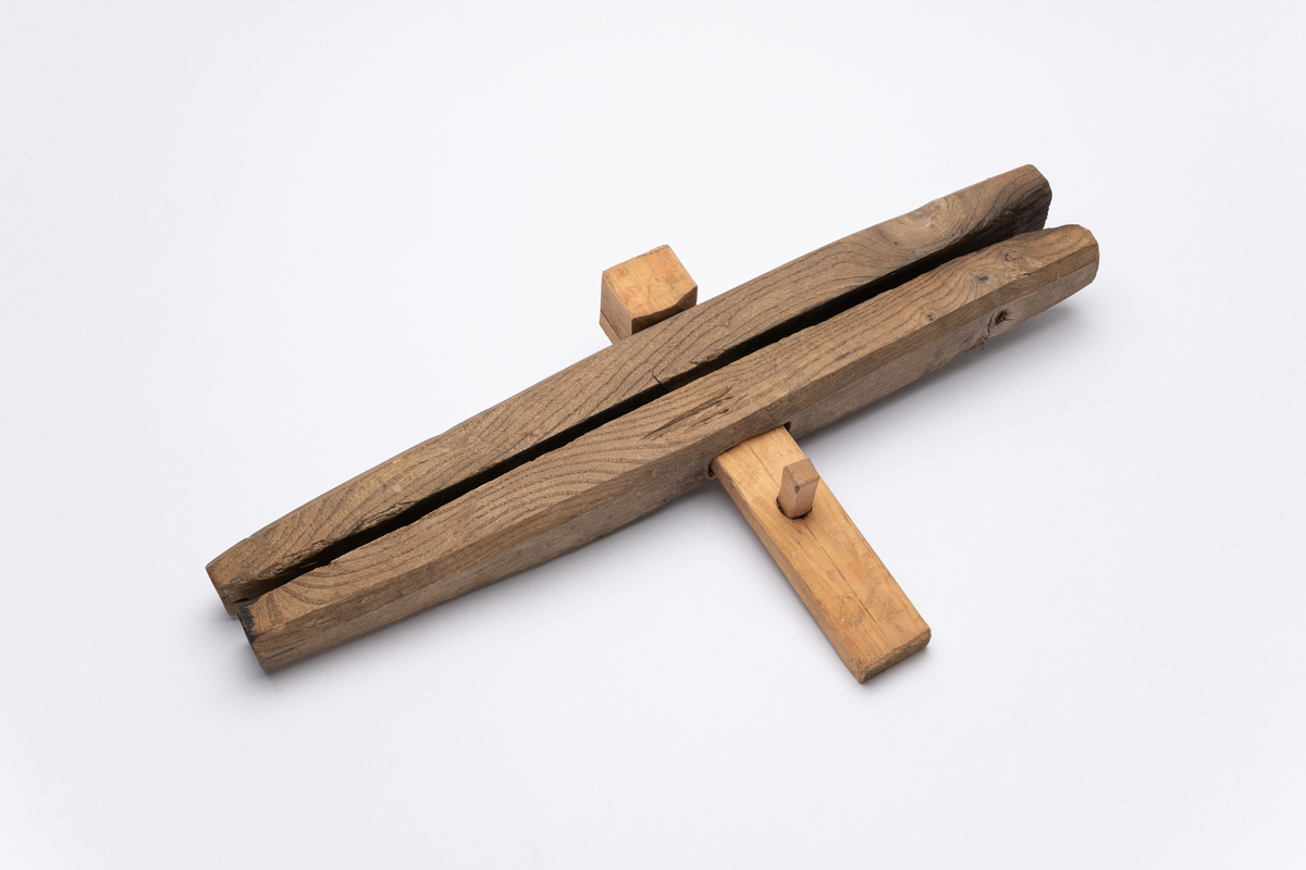 Del av båtklemme i tre. Nyere modell. Brukt til å holde bordgangene sammen ved båtbygging.