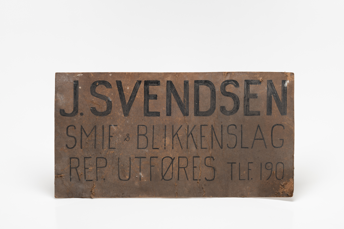Skilt til J. Svendsens smie og blikkenslag på Kirkeøy. Skilt i papp/ sponpapp. Tekst påført med tusj. Et hull i hver ende øverst til feste/ oppheng.