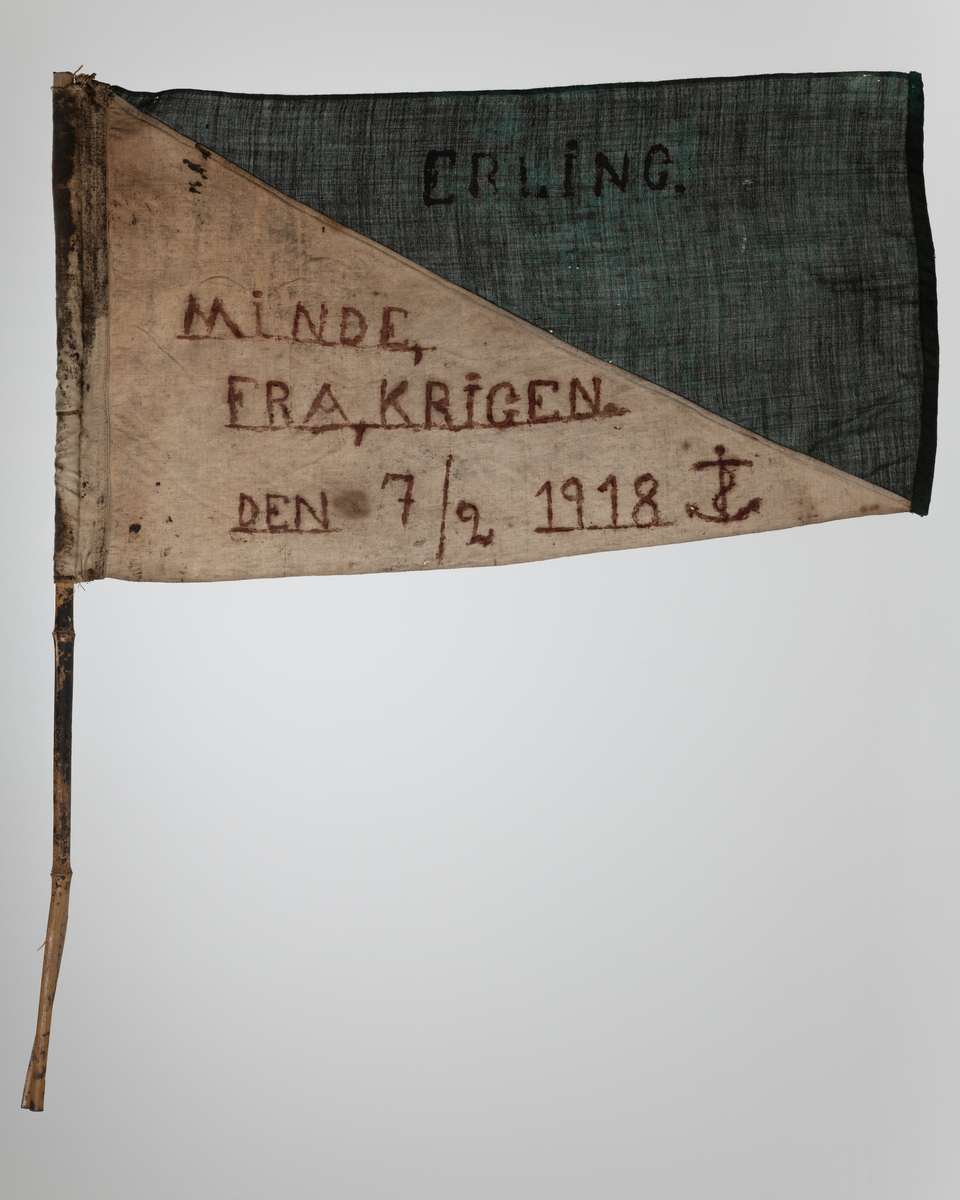 Flagg i lin festet til bambusstang. Bambusstangen er sprekt/ flisete i enden. Flagget er sydd rundt stanga. Flagget er todelt, delt diagonalt. Øverste del er malt grønn. Navnet "Erling" er malt på. Nederste del er ufarget (naturhvit). Tekst malt på: "Minde fra krigen den 7/2 1918".