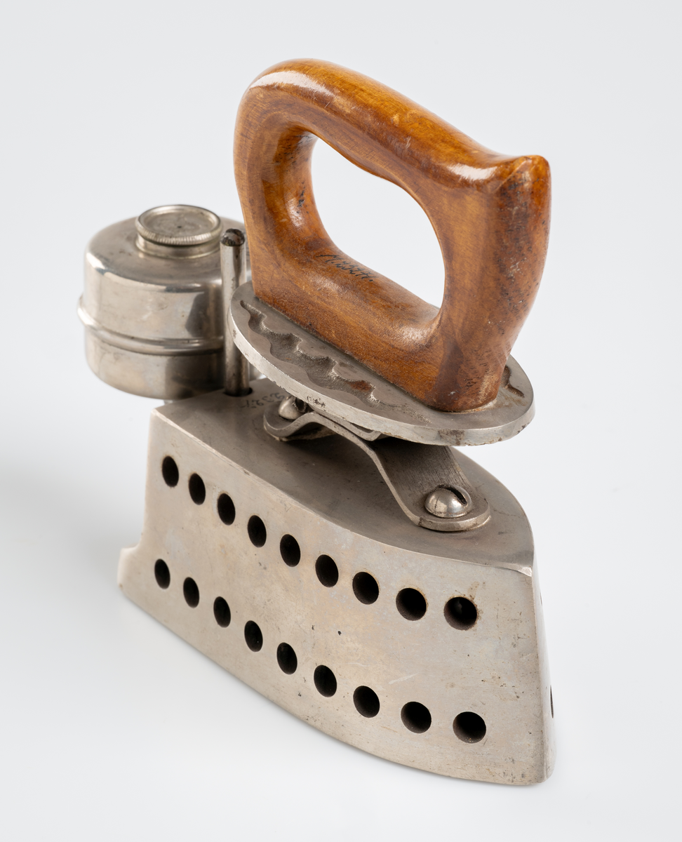 Strykjärn, pressjärn, med oljebehållare för uppvärmning. Trähandtag.

Inskrivet i huvudkatalog 1975.