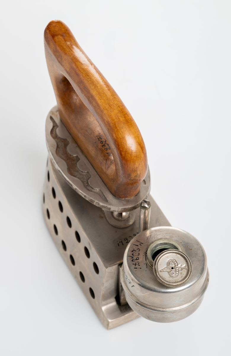 Strykjärn, pressjärn, med oljebehållare för uppvärmning. Trähandtag.

Inskrivet i huvudkatalog 1975.