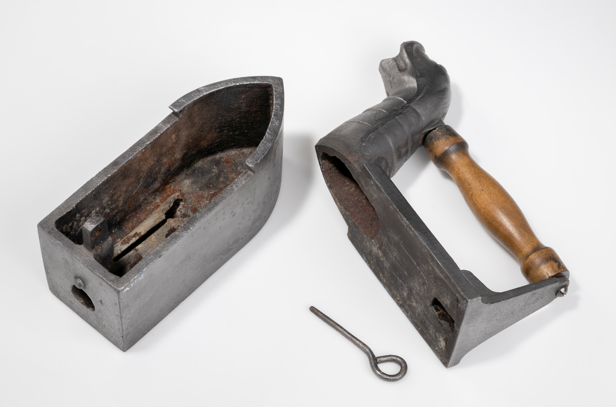 Dekorativt strykjärn, pressjärn, av järn med kolbehållare. Utformat med djurhuvud. Handtag av trä. Tillhörande strykjärnsställ av järn.