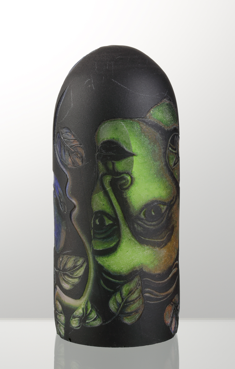 Graalämne till skål av Eva Englund. Grönt, orangea, svart med suggestiva ansiktsmotiv.