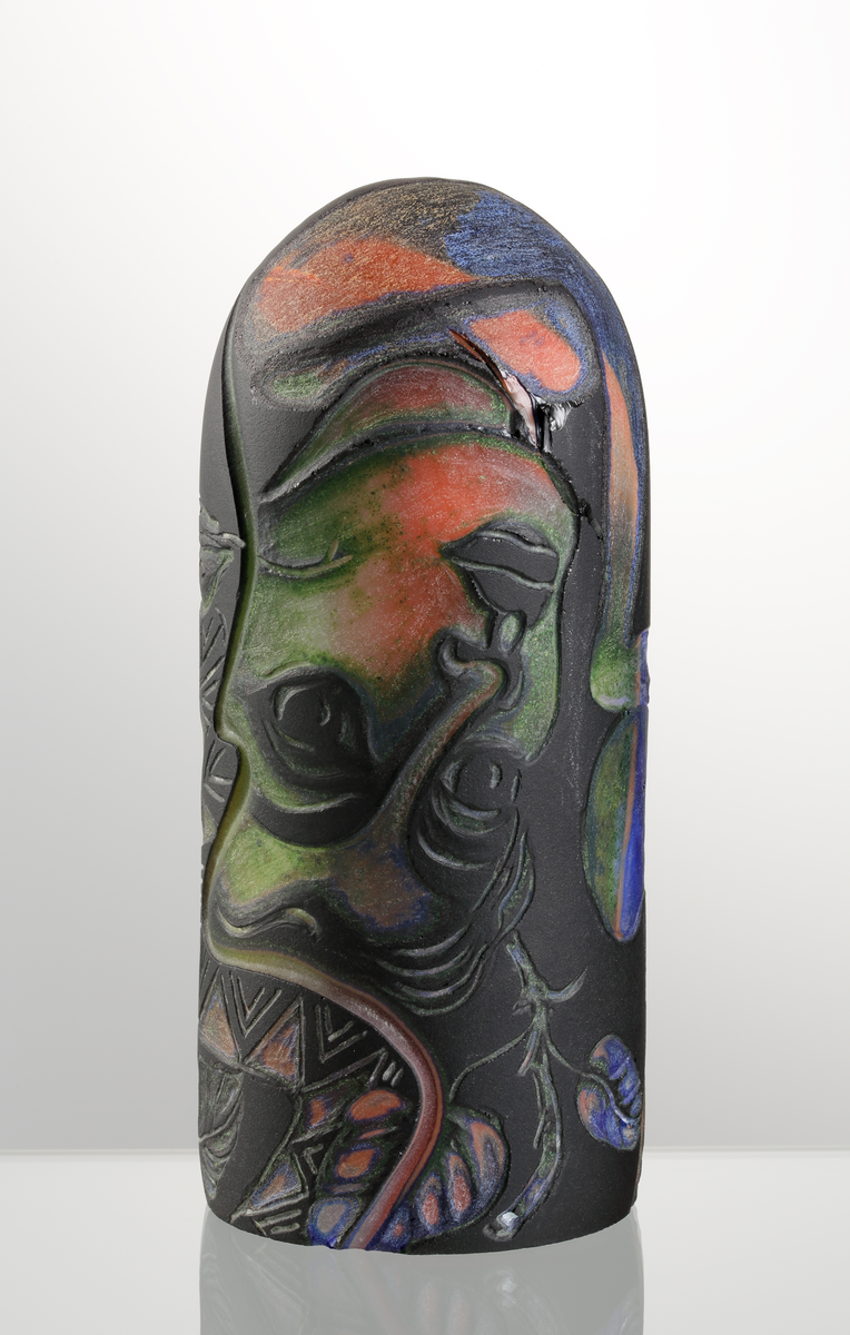 Graalämne till skål av Eva Englund. Grönt, orangea, svart med suggestiva ansiktsmotiv.