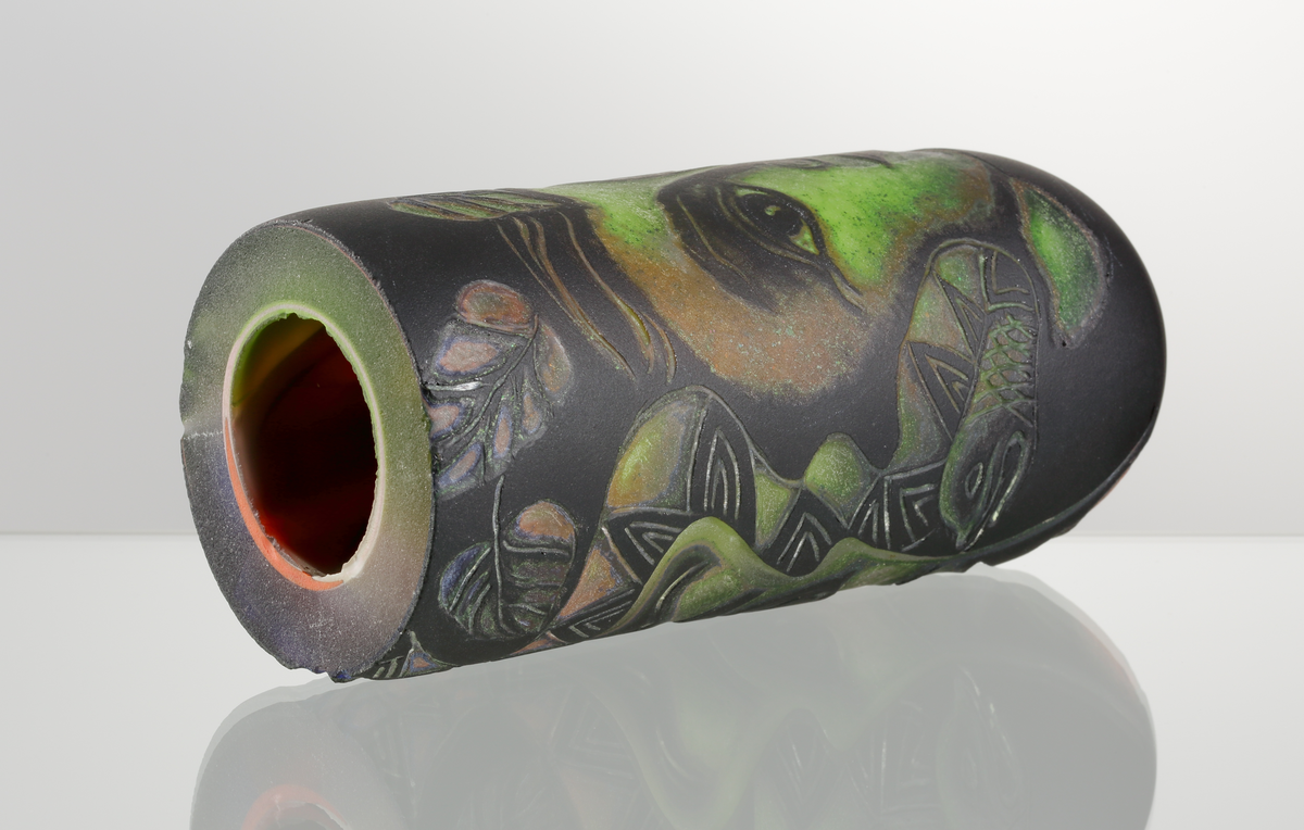 Graalämne till skål av Eva Englund. Grönt, orangea, svart med suggestiva ansiktsmotiv.