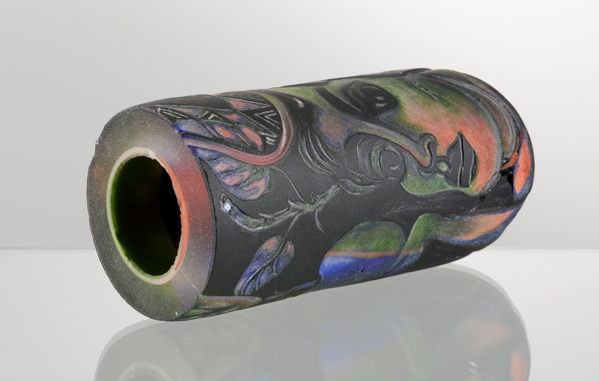 Graalämne till skål av Eva Englund. Grönt, orangea, svart med suggestiva ansiktsmotiv.