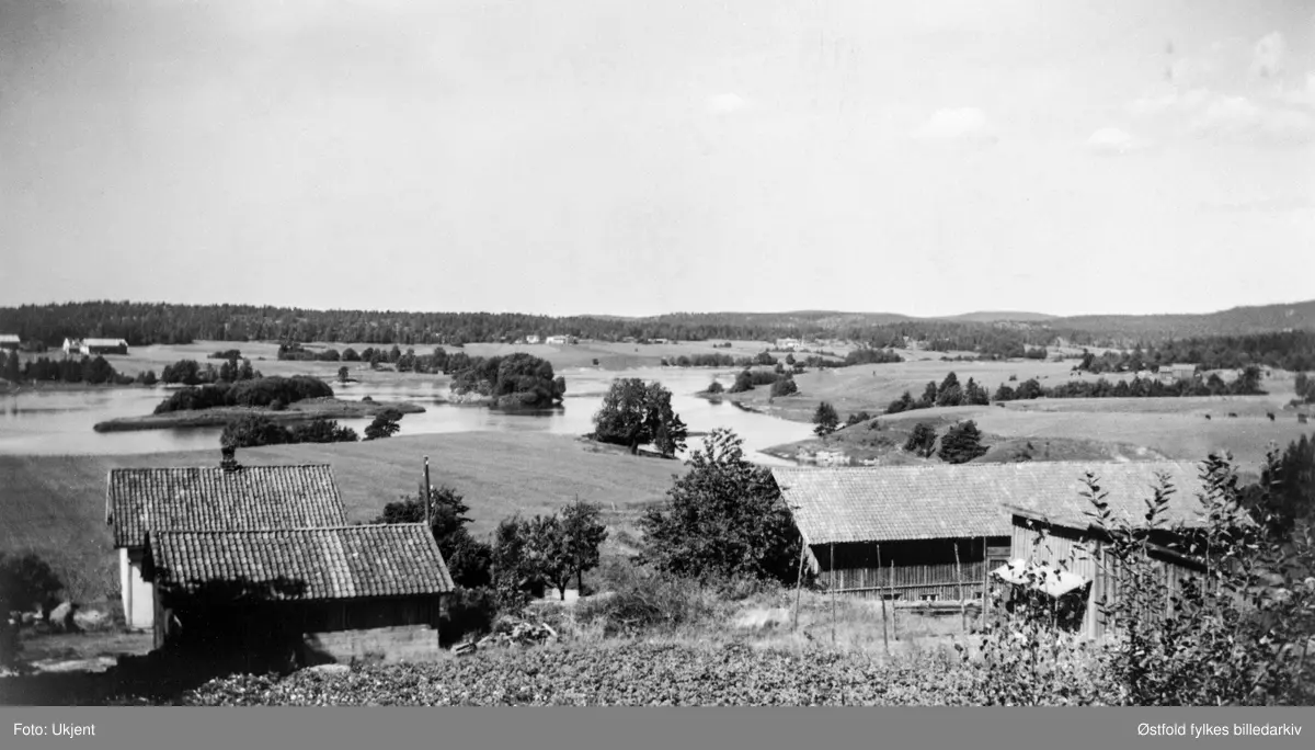 Utsikt over Glomma tatt fra gården Kindalen i Varteig ca. 1955. Holmen tilhører Strømnes, Smaaberg og Vestgaard. I bakgrunnen Tune; gårdene er fra venstre: Strømnes, Blakkestad og Rød. Bildet er tatt ca. 1955.