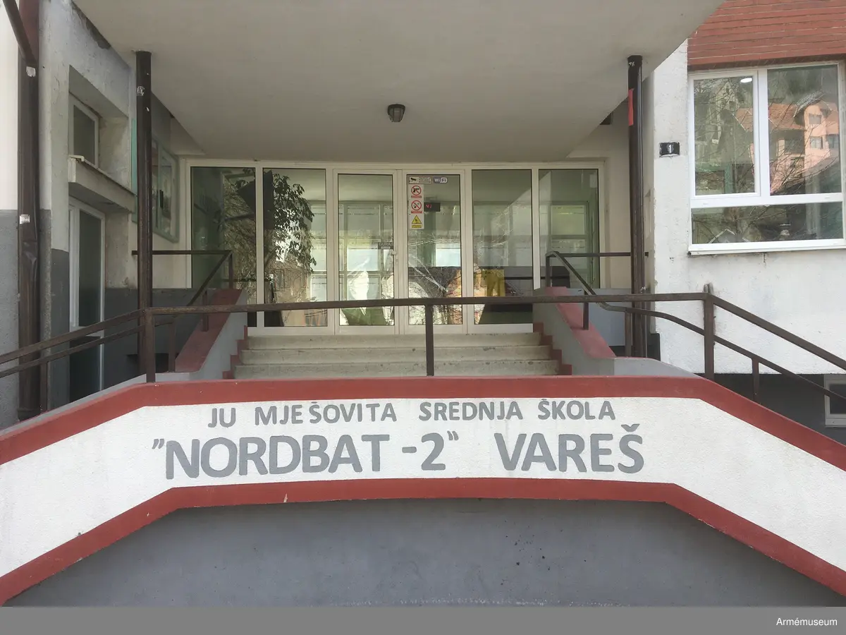 Metallplatta med inskription som varit fäst på insidan av ett fönster på gymnasieskolan Goran Kovacic i Vares i Bosnien. Under 1994 döptes skolan om till ”Nordbat 2” efter de händelser som tidigare tilldrog sig i och omkring skolan där delar av den svensk-danska pansarskyttebataljonen som ingick i UNPROFOR befann sig. Nordbat 2 ingick i BA01 som var den första av de svenska bosnienbataljonerna för de fredsbevarande styrkorna. 

På baksidan av plattan återfinns inskriptioner från elever på skolan. Föremålet förmedlades genom överste Ulf Henricsson och Stig-Inge Blennow.