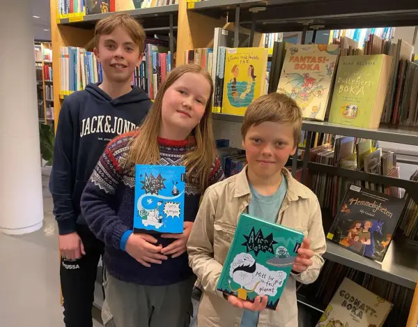 tre gutar framom ei bokhylle, to av dei held kvar si bok av Vegard Markhus