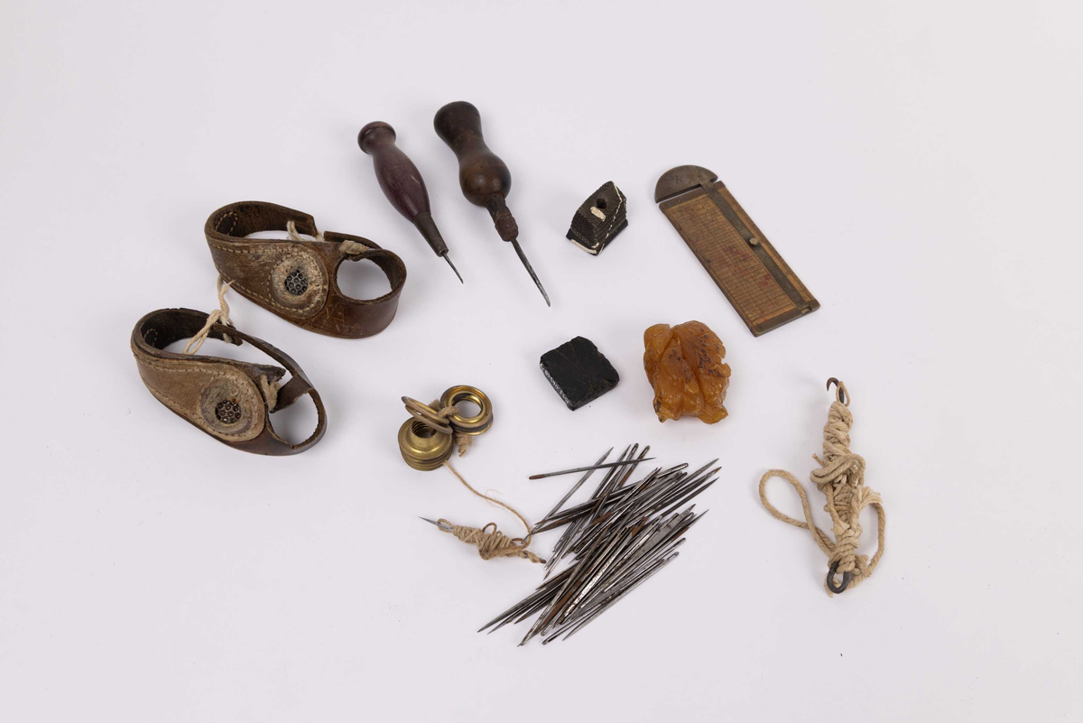 Diverse seilmakerverktøy. Seilmakerhanske/likhanske (2 stk.), syl (2 stk.), maljer  (11 stk.), nåler (ca.40 stk), fettklump, voksklump og seilkrok med tau. Målestav/skyvelær. 
