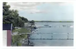 Handkoloreratvykort som avbildar landskap vid havet; bryggor