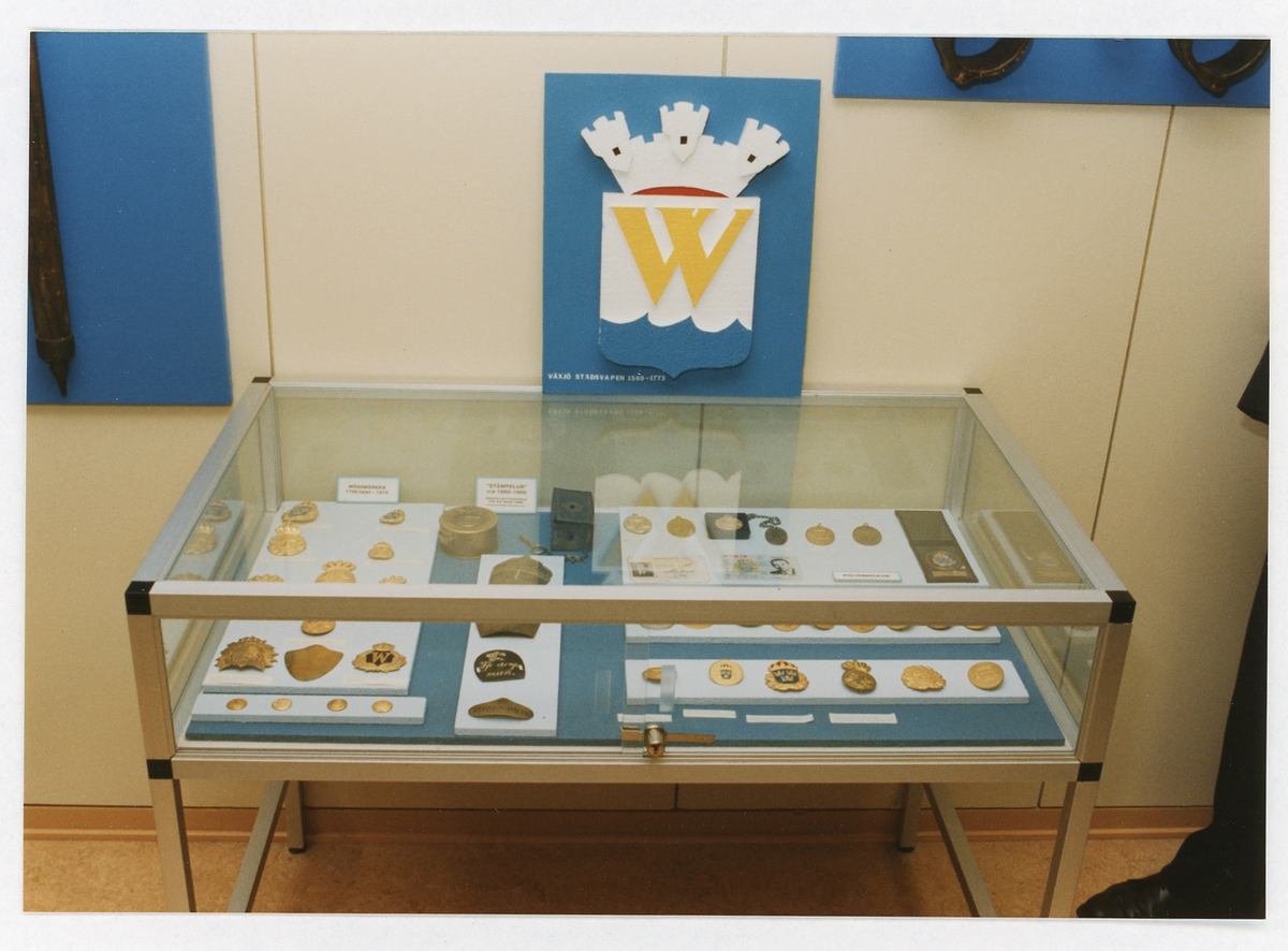 Polismuseet, Växjö. Interiör med monter innehållande diverse mössplåtar, mössmärken, knappar m.m., 1992.