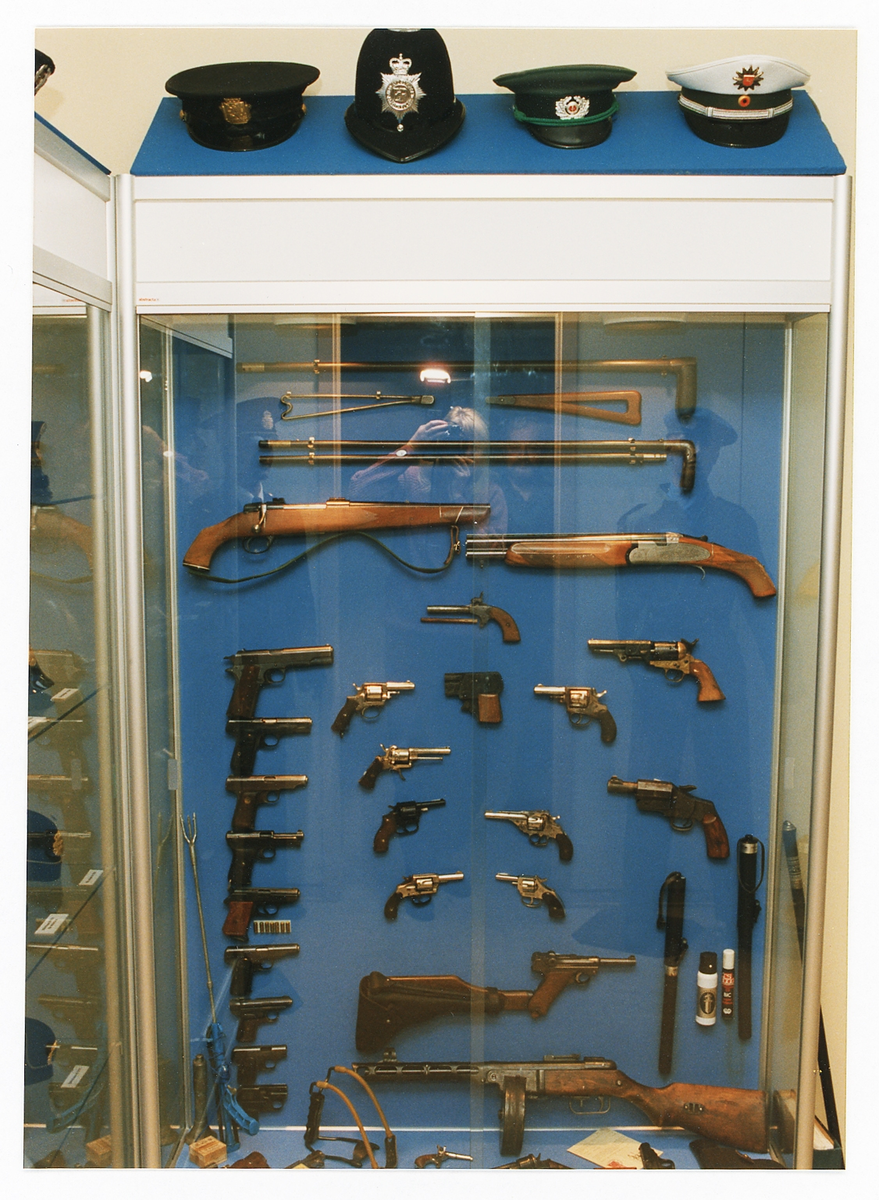 Polismuseet, Växjö,1992. Interiör med monter innehållande diverse olika stick- och skjutvapen. Ovanpå montern syns några olika utländska polismössor.