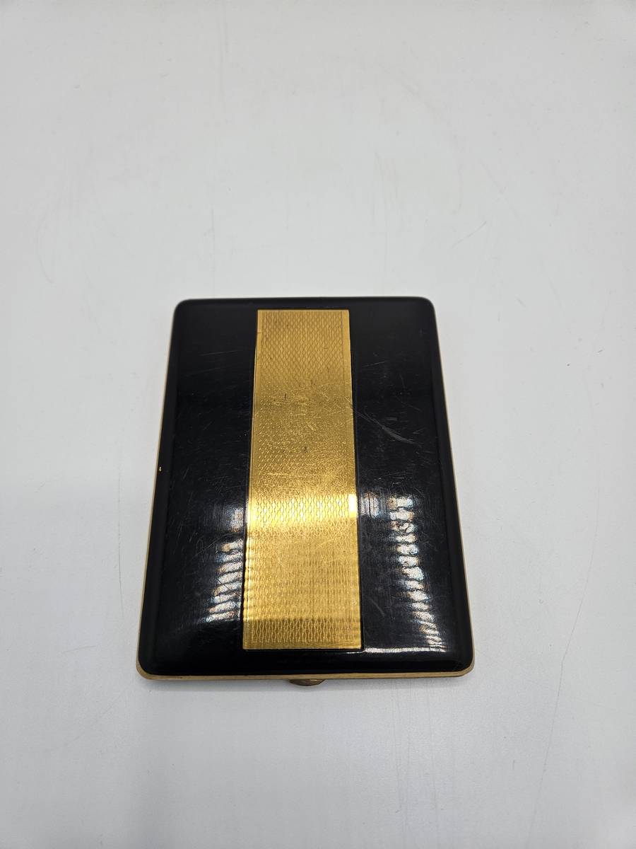 Cigarrettetui av mässing. Svart lackerad med ett guldfärgat rektangulärt fiskfjällsmönster på ovansidan. Stämplat; FOREIGN.  Längd; 10,8 cm. Bredd; 8 cm. Tjocklek; 0,9 cm.  Gåva av dir. S Ekroth, mars 1968.