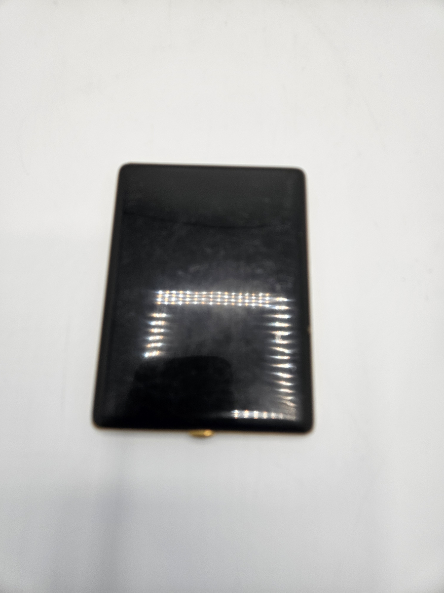 Cigarrettetui av mässing. Svart lackerad med ett guldfärgat rektangulärt fiskfjällsmönster på ovansidan. Stämplat; FOREIGN.  Längd; 10,8 cm. Bredd; 8 cm. Tjocklek; 0,9 cm.  Gåva av dir. S Ekroth, mars 1968.