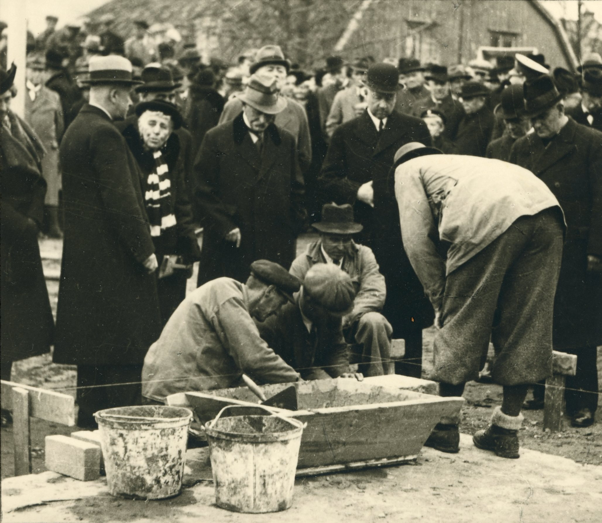Grundstenen för Gävle Museum lägges 26 oktober 1938. Några byggnadsarbetare är i färd med att slutföra arbetet för dagen. Borgmästare Nils Berlin m.fl. övervakar arbetet.