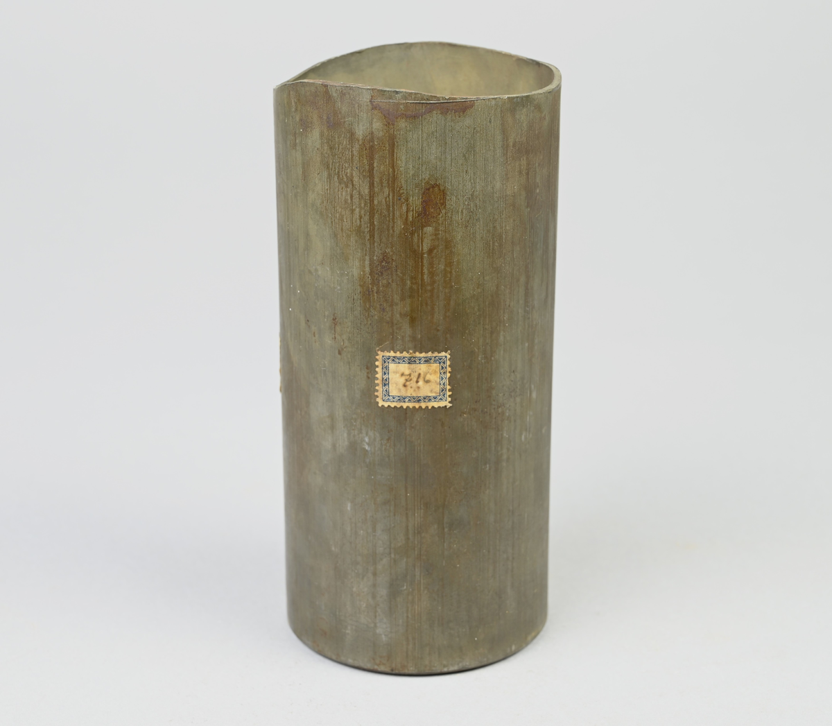 Prov på projektilhylsa. Del av tillverkningsserie. Pressad av stål från runt plåtämne vid Skultuna bruk. Märkning på provet med tejbit med notering: "H-6", samt med etikett med notering: "716".