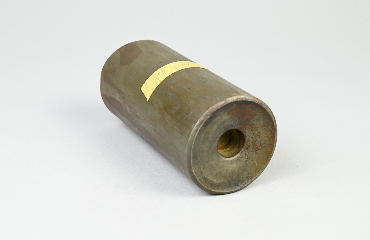 Prov på projektilhylsa. Del av tillverkningsserie. Pressad av stål från runt plåtämne vid Skultuna bruk. Märkning på provet med tejbit med notering: "H-6", samt med etikett med notering: "716".