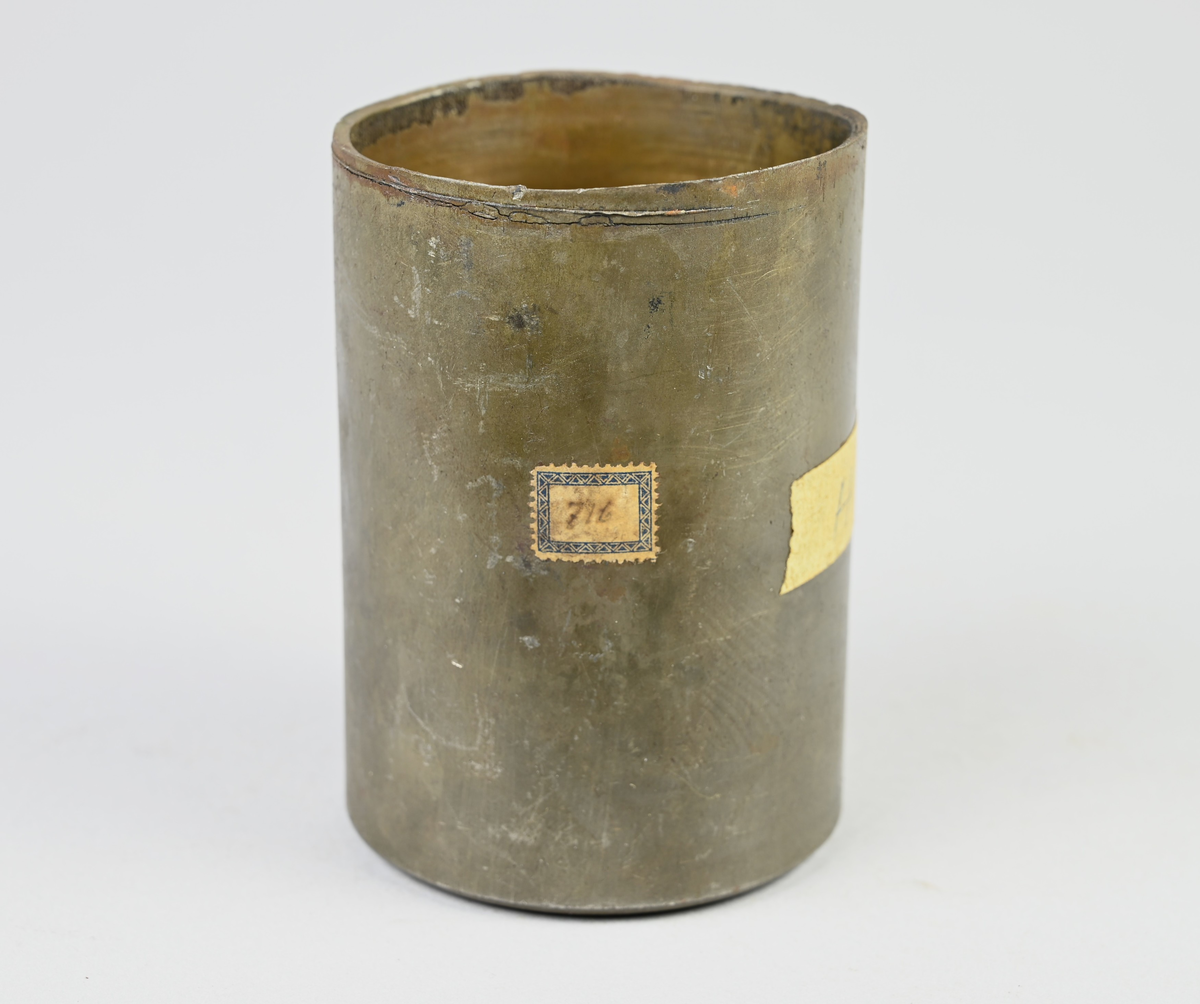 Prov på projektilhylsa. Del av tillverkningsserie. Pressad av stål från runt plåtämne vid Skultuna bruk. Märkning på provet med tejbit med notering: "H-5", samt med etikett med notering: "716".